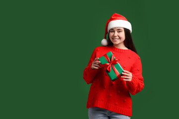 Beautiful woman in Santa hat with Christmas gift on green background. Space for text