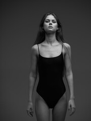 Fototapeta premium Black and white portrait of a young woman in a black bodysuit with serious expression and long hair against a dark background.