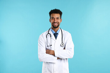 Fototapeta premium Smiling doctor in medical uniform with stethoscope on light blue background