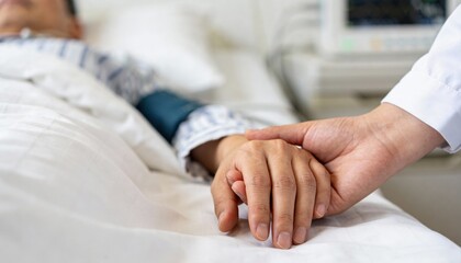 Close up of a patient's hand resting on a hospital bed, being held and comforted by a doctor or nurse's hand.