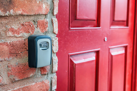 Key lock box with a combination lock mounted on a brick wall, providing secure access next to a vibrant red door