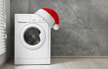 Santa hat on washing machine near grey tiled wall in room