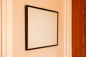 Fototapeta premium Blank white square frame hangs on a peach colored wall, offering copy space for art, advertising, and home decoration