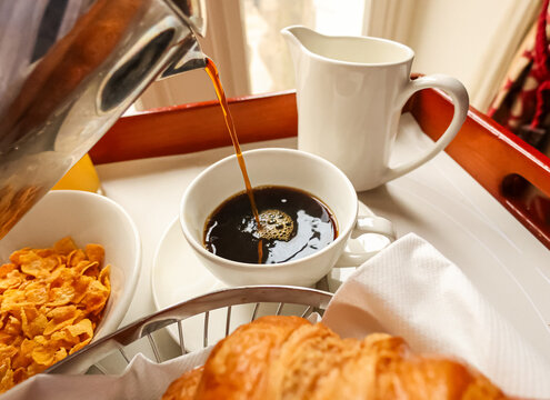 Pouring fresh coffee into a cup on a breakfast tray, enjoying room service at a hotel in London