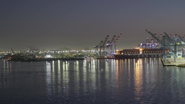 LA, CA, USA. December 18, 2025: A tranquil night view of the Port of Los Angeles with illuminated cranes and a cargo ship reflecting on calm water