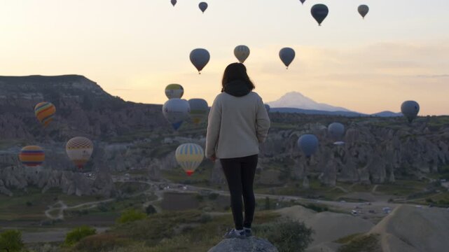 Woman enjoying sunrise view with hot air balloons with Erciyes Mountain in the background in Cappadocia, Turkey