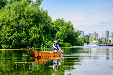 A woman paddles a canoe across still water near a marina on the Toronto Islands, combining summer recreation with scenic waterfront views and relaxed outdoor leisure.