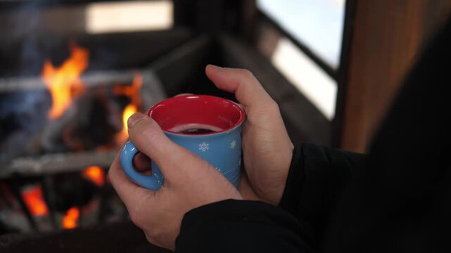 Hands holding a warm mug near a fireplace, creating a cozy winter atmosphere. Concept of warmth, comfort, relaxation, hygge lifestyle, slow living, and emotional well-being during the cold season