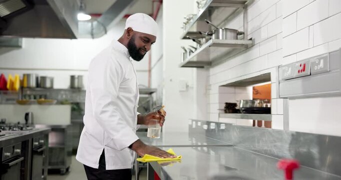 Chef, cleaning and man with cloth, kitchen and sanitary with chemical, smile and surface maintenance. Wiping, workstation and person with spray for disinfection, hygiene and food safety in restaurant - Powered by Adobe