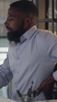 Black man, back pain and stress at office with injury, bad posture and muscle fatigue at startup. African person, spine inflammation and exhausted with burnout, frustrated or ache at creative agency