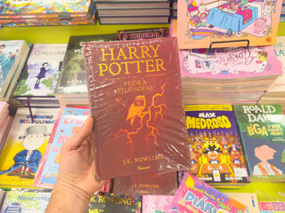 Naklejka premium BELO HORIZONTE, MG, BRAZIL, DECEMBER 12, 2025 A new, plastic-wrapped edition of Harry Potter and the Philosopher's Stone is held in hand at a vibrant bookstore.
