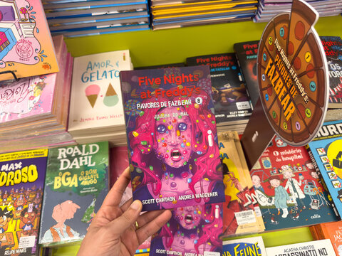 BELO HORIZONTE, MG, BRAZIL, DECEMBER 12, 2025 A hand holds a 'Five Nights at Freddy's' book, showcasing popular children's and young adult fiction in a colorful bookstore setting.
