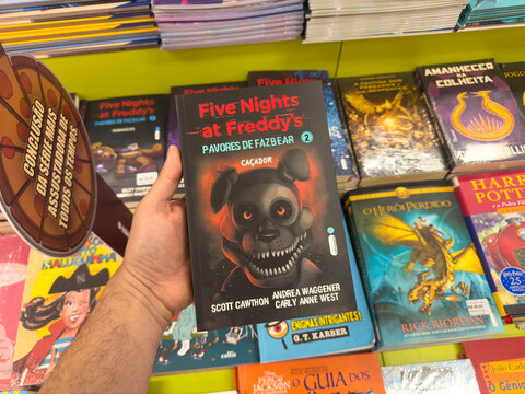 BELO HORIZONTE, MG, BRAZIL, DECEMBER 12, 2025 A hand holds a 'Five Nights at Freddy's' horror book in a vibrant bookstore setting, highlighting popular youth literature.