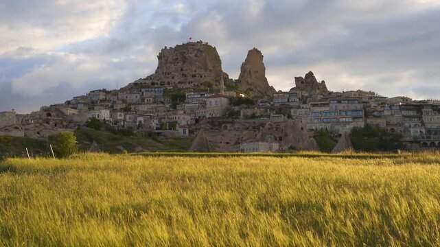 Uchisar town carved into rock formations with buildings and a golden field foreground in Cappadocia, Turkey