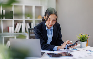 Fototapeta premium Woman doing calculations seated at desk with bills and computer, using calculator while analyzing financial documents, including charts and data tables, busy in planning, budgeting, data analysis 