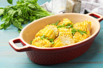 Pieces of grilled corn cobs with green onions on blue wooden table, closeup
