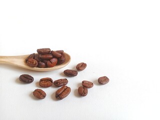 Roasted coffee beans on wooden spoon on white background with copy space