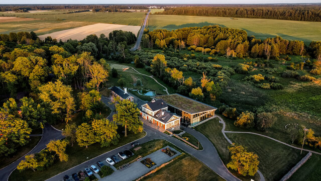 Aerial view of Paliesius Manor in Lithuania surrounded by lush forests, fields, and countryside roads at golden hour, showcasing historic estate architecture, rural landscape, and peaceful Baltic natu