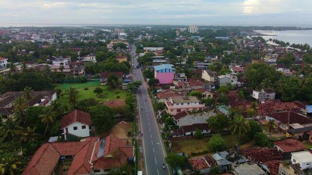 Early morning aerial drone footage flying over the main street of Negombo, Sri Lanka. Quiet city road with light traffic, tropical urban environment and soft sunrise light