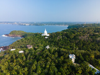 Aerial drone photo of lush tropical jungle with a Buddhist stupa at Rumassala hill overlooking the Indian Ocean in Unawatuna, Sri Lanka. Sacred pagoda surrounded by dense greenery with ocean coastline