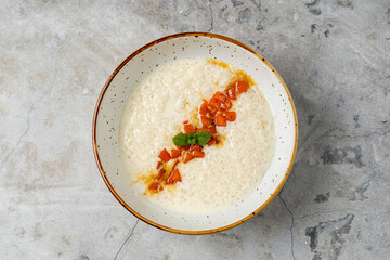 A rustic bowl holds creamy rice pudding, garnished with vibrant pieces of fresh mango and a sprig of mint. The setting captures a delightful dessert experience