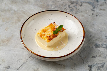 Creamy custard topped with a golden crust rests elegantly on a rustic plate, glistening with sauce and garnished with a fresh mint leaf, inviting all to indulge © Tkachenko Alexey