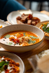 Aromatic curry fills a bowl surrounded by fresh herbs and spices, sharing the table with various flavorful plates in a welcoming restaurant atmosphere