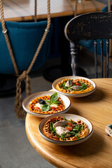 Three colorful plates filled with delicious food rest on a warm wooden table in a charming eatery. The cozy ambiance invites culinary exploration and shared enjoyment