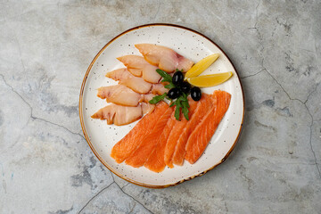 Vibrant slices of salmon and white fish rest artfully on a plate, accented with olives and lemon. This delightful arrangement showcases skilled culinary art, inviting a culinary adventure
