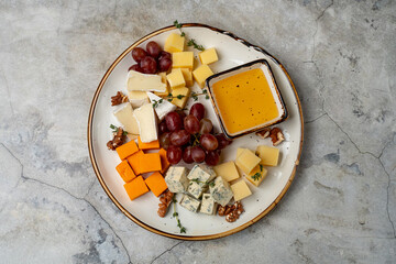 Colorful assortment of cheeses served on a rustic plate, accompanied by fresh grapes and a small bowl of honey, creating a perfect snack for an afternoon gathering