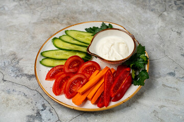 Colorful slices of cucumber, tomato, and carrot are beautifully arranged on a plate beside a small bowl of creamy dip. Perfect for sharing at a friendly gathering or enjoying alone