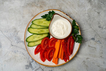 A vibrant selection of cucumbers, carrots, red bell peppers, and cherry tomatoes is arranged on a plate, accompanied by a creamy dip. Perfect for a healthy snack or gathering