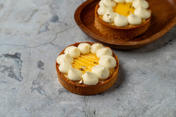 On a textured stone surface, a beautifully crafted citrus tart showcases vibrant yellow filling topped with soft cream and touches of edible gold. The rustic wooden plate adds warmth to the scene