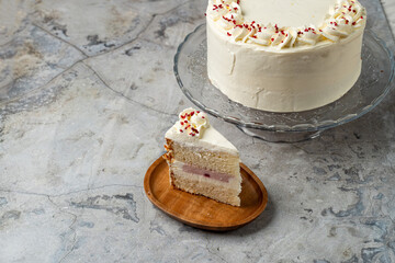 A beautifully decorated white cake sits on a glass stand, showcasing its creamy frosting and delicate raspberry filling. A slice reveals its layers, inviting taste