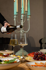 A person pours sparkling wine into a glass as a candlelit table displays a colorful array of appetizers. The atmosphere feels warm and inviting, perfect for a gathering