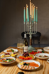 A beautifully arranged table showcases an array of colorful dishes, fruits, and a bottle of wine. Candles illuminate the setting, enhancing the warm, inviting atmosphere