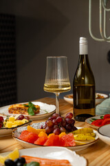 Friends enjoy a lively celebration around a wooden table adorned with colorful fruits, savory dishes, and elegant wine, creating a warm and inviting atmosphere
