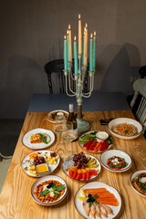 Guests gather around a wooden table adorned with elegant dishes, showcasing vibrant salads, fresh seafood, and a variety of fruits, all complemented by flickering candlelight