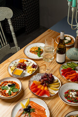 A warm and inviting table displays an array of colorful dishes, from fresh fruits and seafood to savory cheeses, alongside a chilled bottle of wine. Friends enjoy their culinary feast