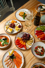 Colorful plates filled with seafood, cheeses, and fruits surround elegant glasses and a wine bottle, creating a warm and inviting dining experience during a charming gathering