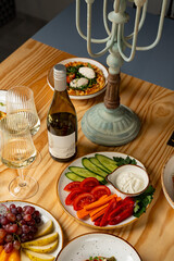 A charming table scene features an array of fresh vegetables, a bottle of wine, and glasses, creating a warm atmosphere for sharing delicious moments with friends