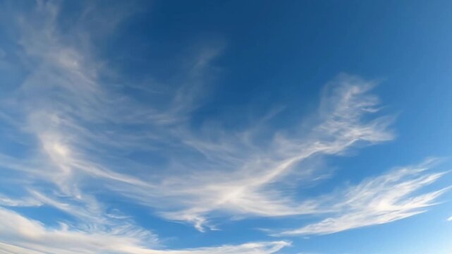 A breathtaking wide shot of a pristine blue sky adorned with delicate, wispy white cirrus clouds gracefully drifting across the expanse. The ethereal formations slowly evolve and change shape, creatin
