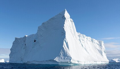 Massive angular iceberg rising from deep blue ocean under a clear sky, dramatic white ice cliffs and sharp peak in a pristine polar seascape