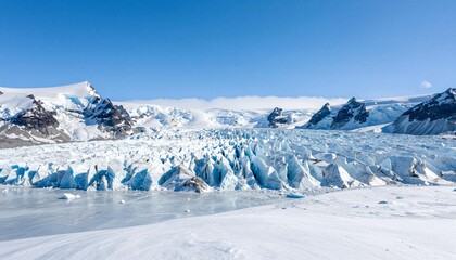 Expansive blue-tinged glacier with jagged ice formations, crevasses, snow-covered mountains and a clear blue sky