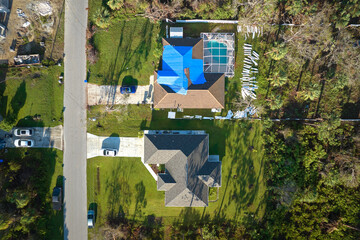 Aerial view of damaged in hurricane Ian house roof covered with blue protective tarp against rain water leaking until replacement of asphalt shingles