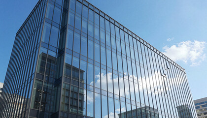 Modern glass office building with reflective blue windows showing sky and clouds, sleek curtain-wall facade in an urban business district