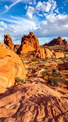 Orange rock formations scattered beneath a blue sky with fluffy white clouds in a desert landscape
