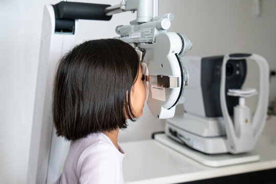 A happy 6-year-old girl undergoes a vision test using a phoropter during a pediatric eye exam at an ophthalmology clinic.