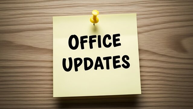 Yellow sticky note pinned to a wooden desk announces important office updates with bold black lettering