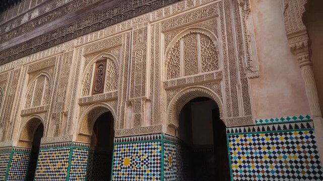 Moroccan riad facade detail, slow pan across intricate carved plaster arches and traditional colorful geometric zellij tiles in soft natural daylight.